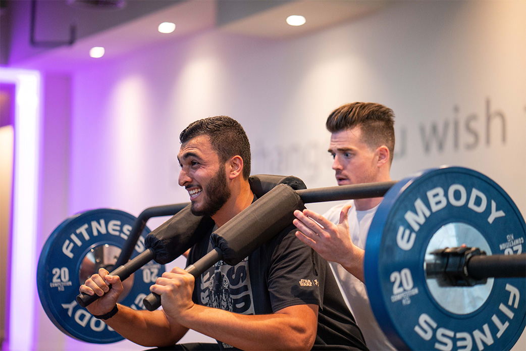 Man lifting weights while being supported by his trainer