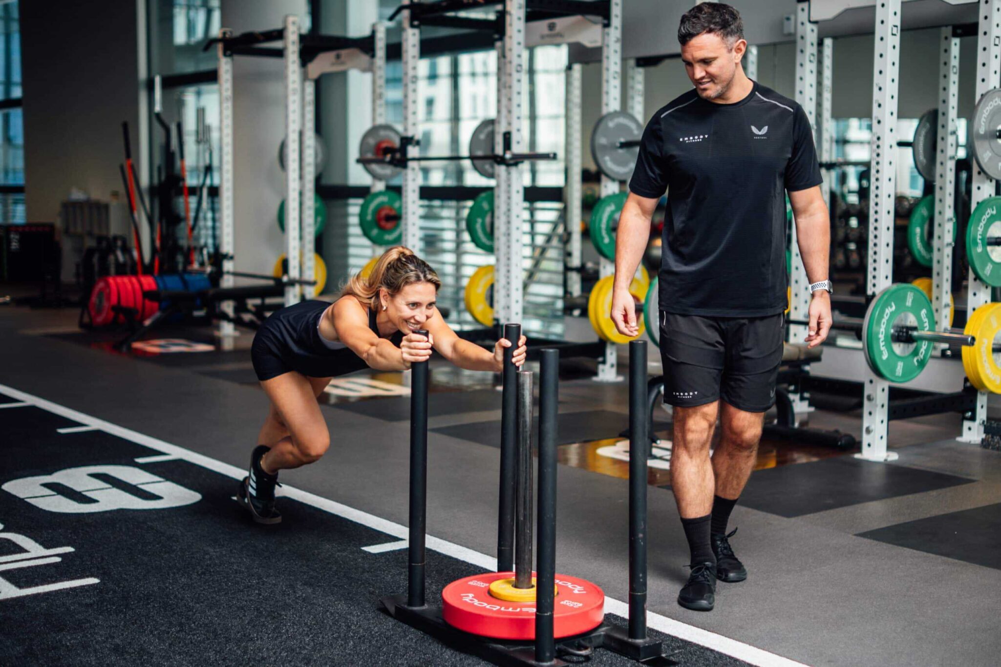 Client pushing weighted sled with her Embody personal trainer Rob