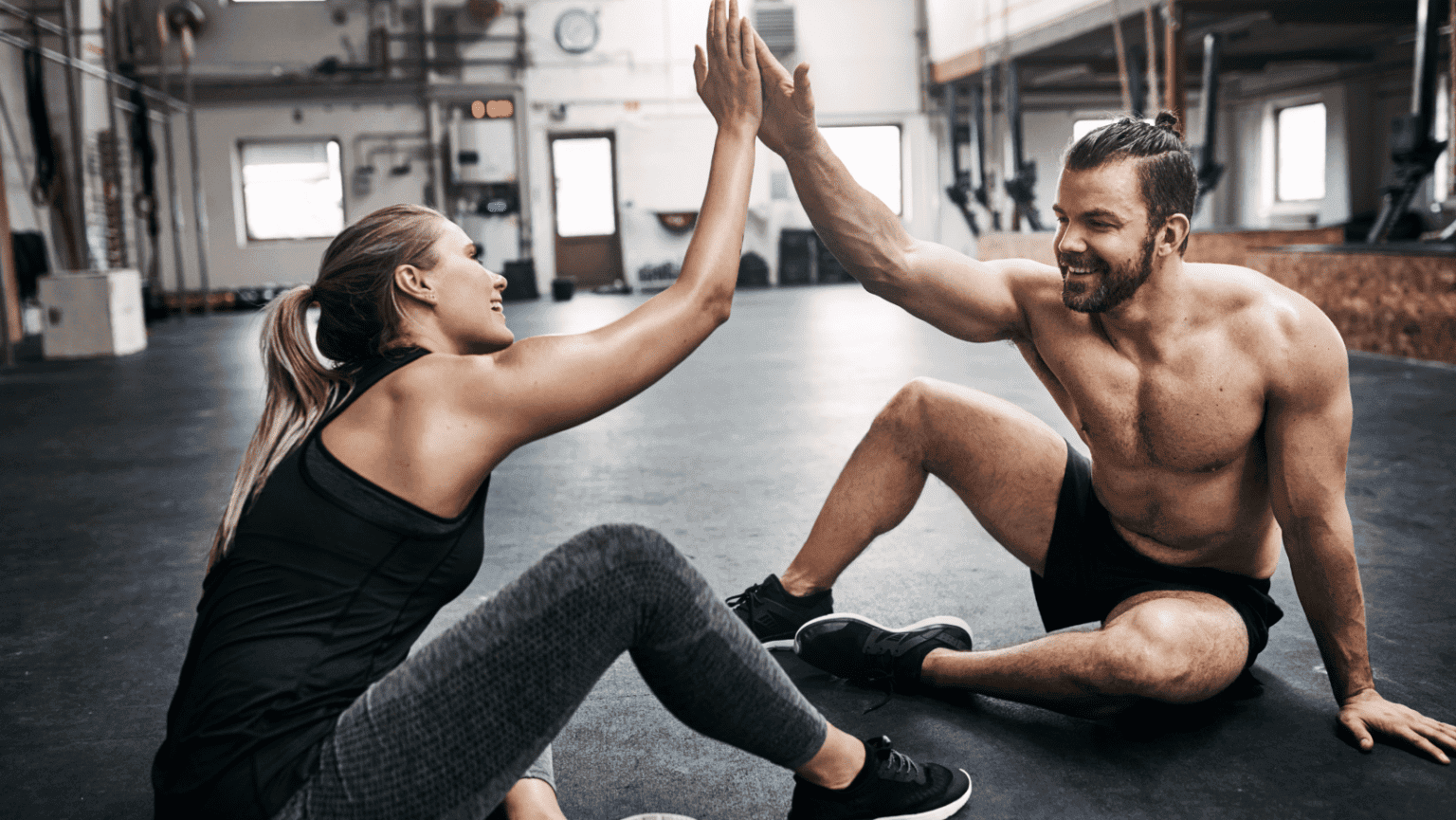 Male and female sitting down and high fiving after workout