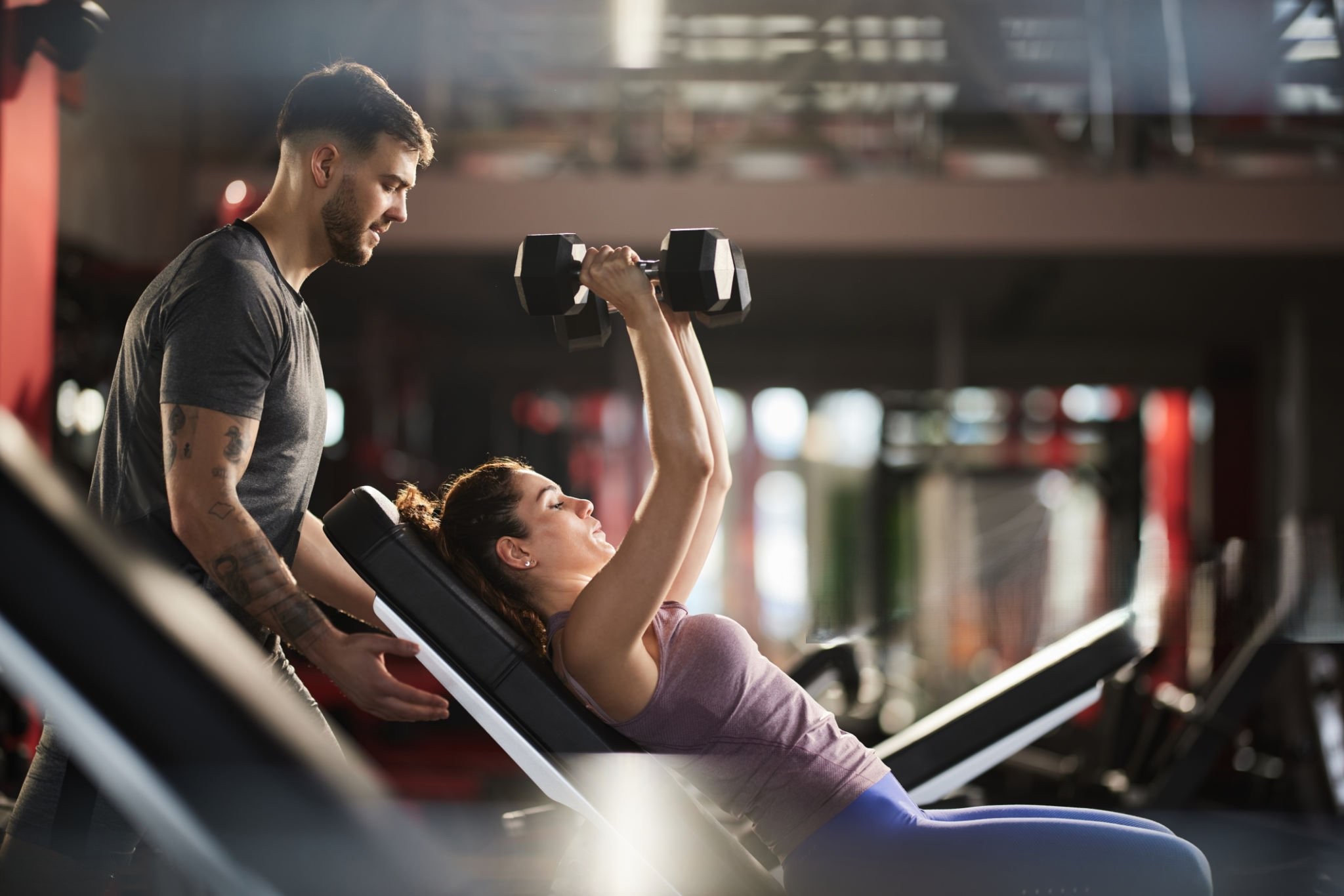 Fitness instructor assisting athletic woman in exercising with dumbbells at gym.